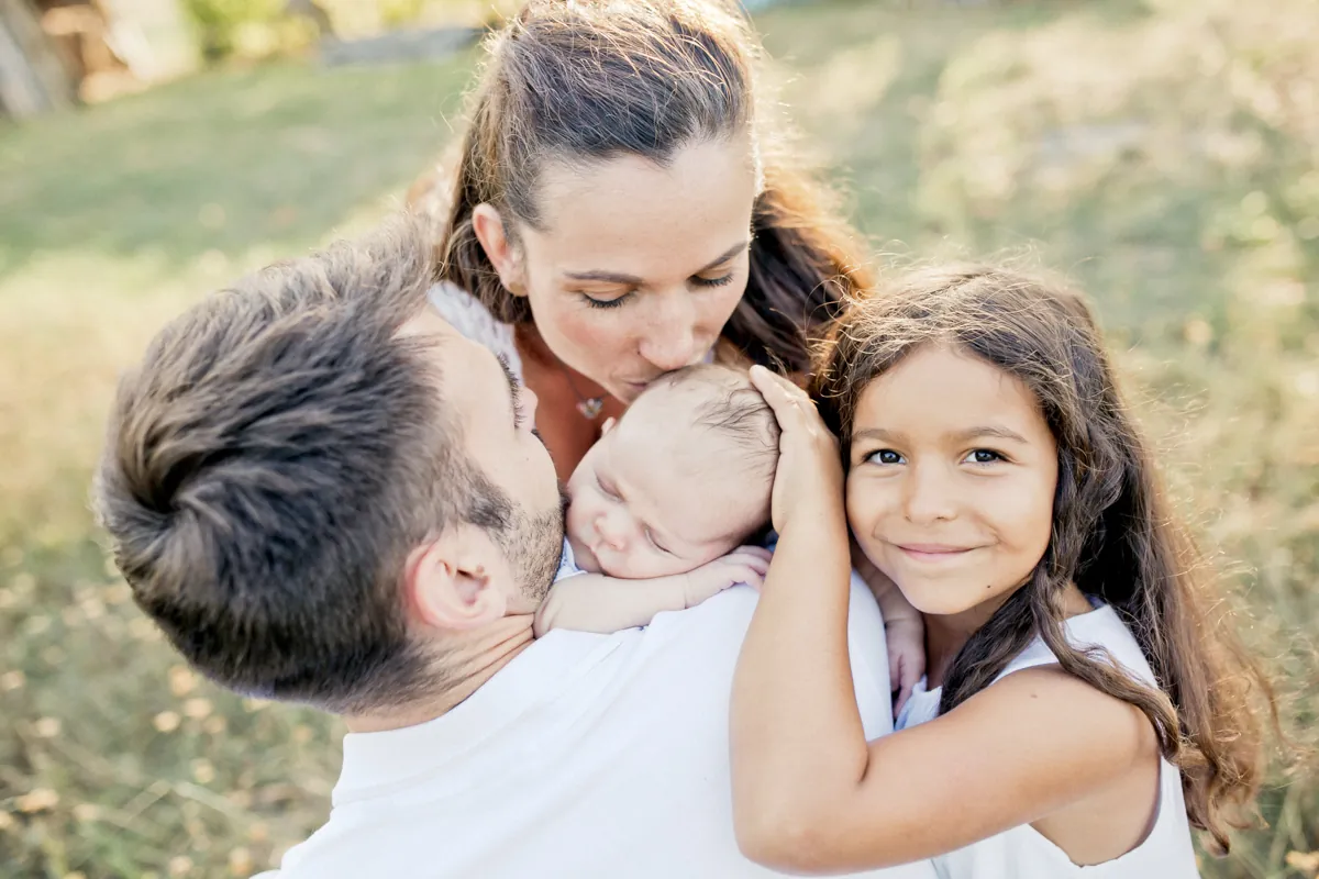 Eltern küssen ihr Baby, Tochter lacht in die Kamera