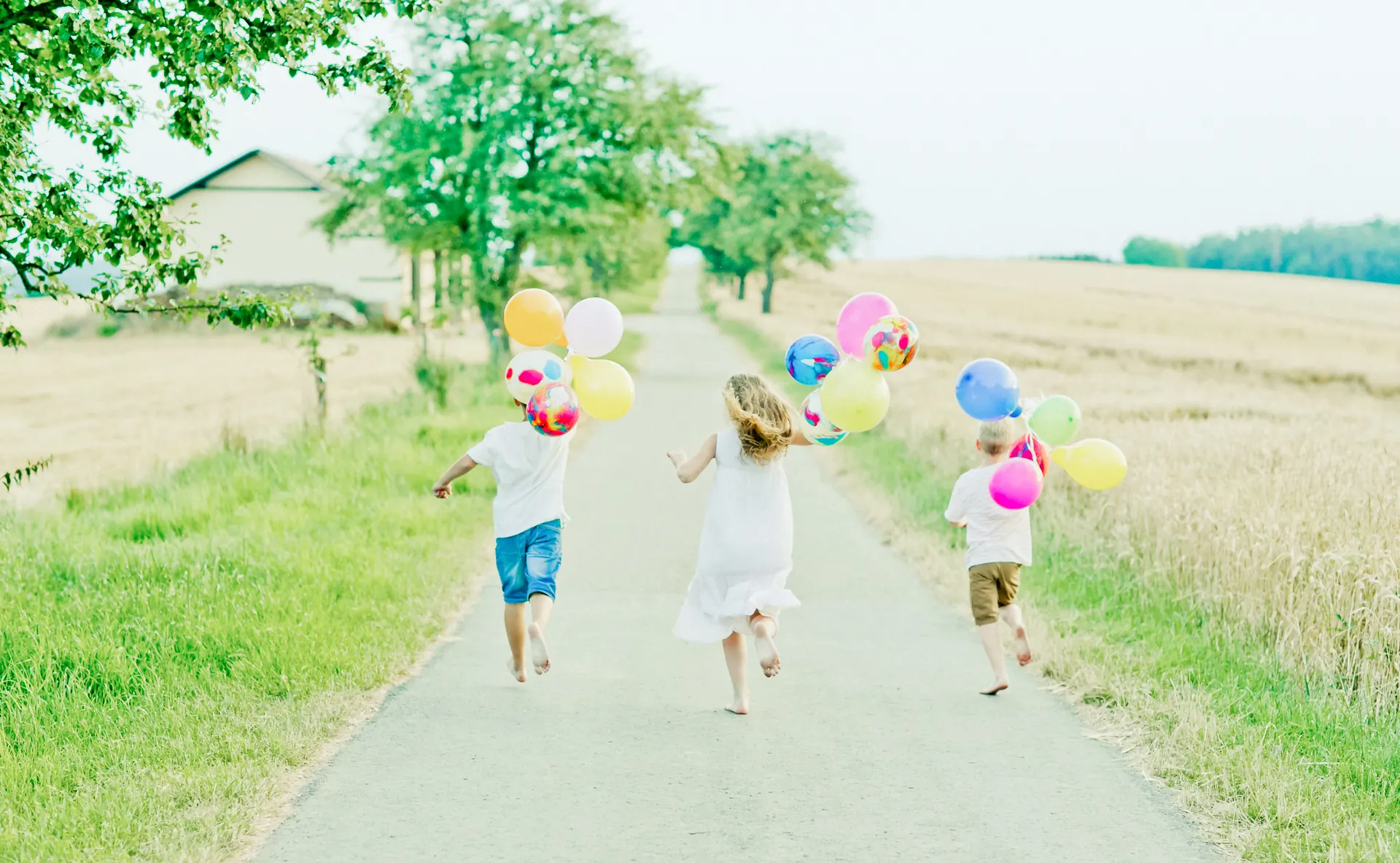 Kinder rennen mit Luftballons über einen Feldweg